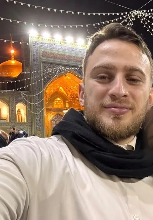 Hadi in a shrine courtyard at night, golden dome behind him